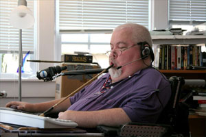 Guy Thomas in his home, typing with the use of assistive technology, a mouth stick.