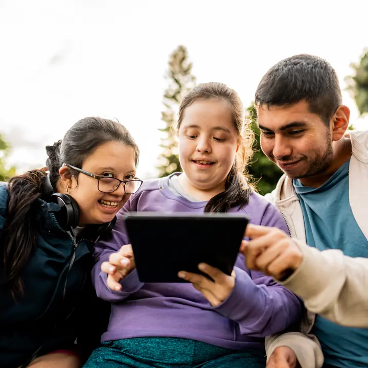 Three young people with disabilities smiling together as they look at a tablet