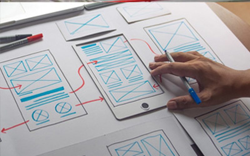 A hand sketching mobile app wireframes on paper